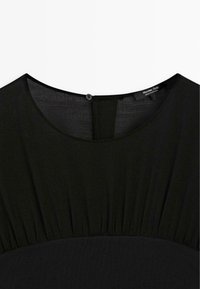 Schwarzes Kleid mit rundem Ausschnitt, gerafftem Stoff an den Schultern und einer Knopfleiste im Rücken. Der Stoff scheint weich und leicht zu sein.