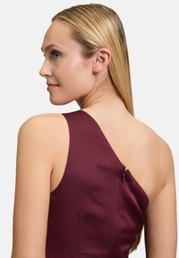 Robe bourgogne en satin, présentant un design à une épaule, un détail de fermeture éclair sur le côté et une texture lisse sur le dos d'un mannequin.