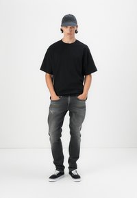 Tricou negru cu mânecă scurtă, blugi gri distresați, adidași negri și o șapcă închisă cu text. Design slim-fit, material din bumbac, stil casual.