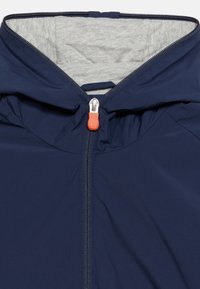 Μπλε σκούρο μπ ουφάν με γκρι εσωτερική επένδυση κουκούλας, εμπρόσθιο φερμουάρ με πορτοκαλί λαστιχένιο τράβηγμα και υφασμάτινη θηλιά στην πίσω πλευρά του γιακά.