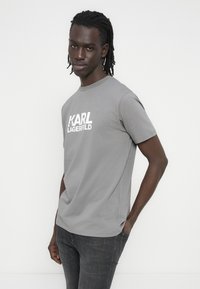 Szary t-shirt z krótkim rękawem wykonany z bawełny, z białym logo "KARL LAGERFELD" umieszczonym na środku klatki piersiowej. Okrągły dekolt, luźny krój.