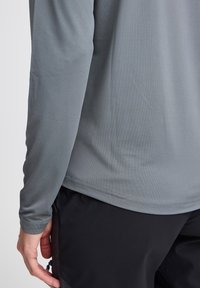Grijs shirt met lange mouwen, gemaakt van een gladde, lichte stof, met een ronde halslijn en een rechte zoom. Draag het met zwarte broek.