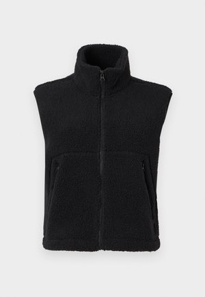 Must muströöp, millel on kõrge krae, ees lukuga ja kaks külge taskut. Omab tekstuurset kangast ja varrukateta disaini.