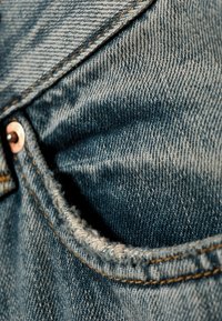 Λεπτομέρεια τσέπης από τζιν που δείχνει μπλε ύφασμα με υφή ύφανσης, αντίθετη πορτοκαλί ραφή και συμπληρωματικό χαλκινο καρφί στο άκρο.