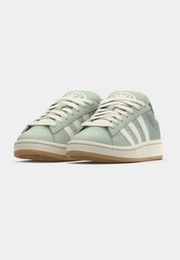 Green suede sneakers featuring white side stripes, beige rubber sole, cream laces, and branded logo on the tongue.