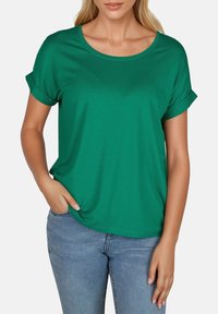 Camiseta verde de manga corta con cuello redondo y puños enrollados, hecha de tela suave, combinada con jeans azules.