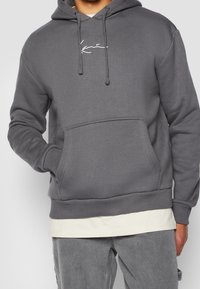 Felpa grigia con tasca frontale, cappuccio con coulisse e logo bianco ricamato sul petto. Realizzata in un tessuto morbido e strutturato.