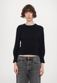 Marineblauer, kurz geschnittener Pullover mit gerippter Textur und langen Ärmeln, kombiniert mit hoch geschnittenen, ausgewaschenen grauen Jeans. Schlichte runde Ausschnittform, keine Verzierungen.