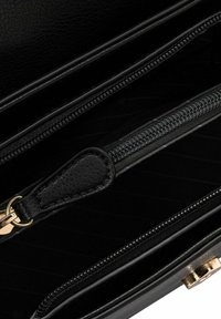 Zwart leren handtas interieur met één ritscompartiment, gestructureerde voering en gouden hardware accenten. Schoon ontwerp met een gladde afwerking.