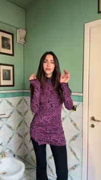 Lila-schwarz gemustertes Langarmoberteil mit Raffung, kombiniert mit schwarzer Hose. Hat einen hohen Ausschnitt und eine schlanke Passform.