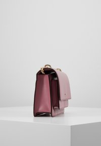 Borsa a mano in pelle rosa con un design strutturato, caratterizzata da una maniglia in catena dorata e due tasche esterne. Texture liscia con bordi a contrasto.