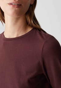 Bordeaux langwerpige shirt met een ronde halslijn en zachte textuur, die een gladde stof en schoudernaad laat zien. Minimale stikseldetails.