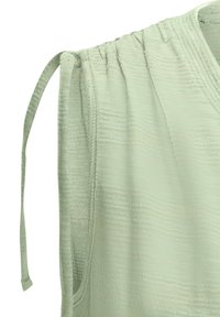 Light green top featuring a textured, woven fabric, with gathered details on the shoulder and a long, thin strap on the left side.