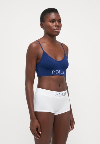 Jūras flotes stila ribota bralette ar regulējamiem siksniņām un "POLO" logo. Balti zēnu šorti ar elastīgu jostu, uz kuras redzams zils "POLO" logo.
