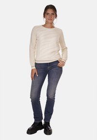 Maglione a maglia beige chiaro con strisce diagonali testurizzate, abbinato a jeans in denim scuri e stivali neri con lacci. Silhouette aderente.
