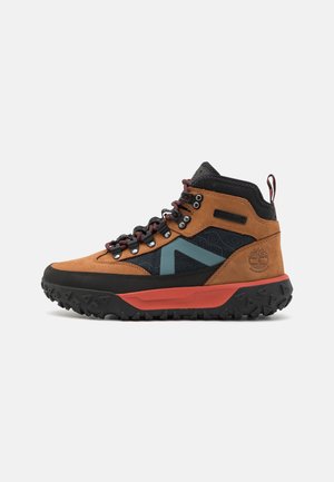 Stivale da trekking marrone e nero con tomaia in suede texture, un accento blu, suola in gomma, intersuola rossa e occhielli in metallo per i lacci.