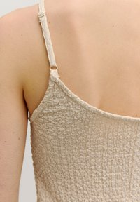 Beiger, strukturierter Stoffoberteil mit verstellbaren Trägern; verfügt über ein gerafftes Design und einen runden Ausschnitt auf der Rückseite.