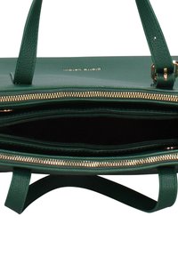 Sac à main en cuir vert avec fermeture éclair ton or. L'intérieur comprend une doublure sombre et plusieurs poches pour l'organisation. Surface texturée.