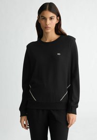 Felpa nera realizzata in tessuto liscio, con scollatura rotonda, maniche lunghe e dettagli con zip ai lati, accompagnata da un piccolo logo sul petto.