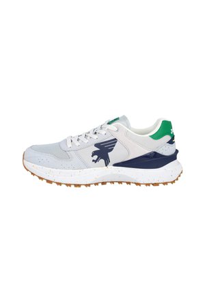 Zapatilla blanca y gris con lengüeta verde en el talón, logo de águila azul marino en el lateral, suela blanca con manchas y suela exterior marrón texturizada.