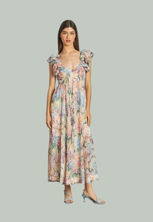 Blumen-Maxikleid mit Rüschensäumen, das in sanften Farben und einem fließenden Design gehalten ist. Kombiniert mit hellblauen Riemchenschuhen.