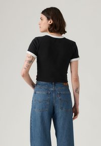 Μαύρο crop top t-shirt με λευκή επένδυση, συνδυασμένο με φαρδιά μπλε τζιν παντελόνια με πίσω τσέπες και λεπτομέρειες με ραφή.