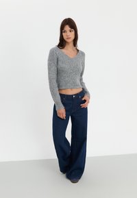 Szary, krótki sweter z dekoltem w serek o prążkowanej fakturze, zestawiony z jeansami z wysokim stanem i szerokimi nogawkami w ciemnoniebieskim kolorze, z widocznymi szwami i kieszeniami.