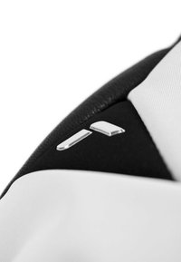Weißer und schwarzer Stoff mit glatter Textur; verfügt über silberne Hardware-Akzente, darunter zwei längliche Knöpfe in einer Ecke.