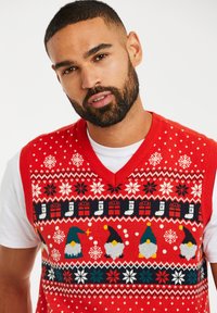 Rode gebreide mouwloze sweater met witte sneeuwvlokken, kleurrijke gnomes en geschenkmotieven, met een V-hals en gedetailleerde patronen.