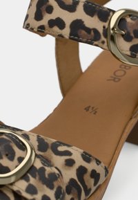 Σανδάλια με λεοπάρ μοτίβο, δύο λουριά, αγκράφα χρυσού χρώματος και εσωτερική σόλα με ανοιχτό καφέ υφή. Το μέγεθος σημειώνεται ως 4½.