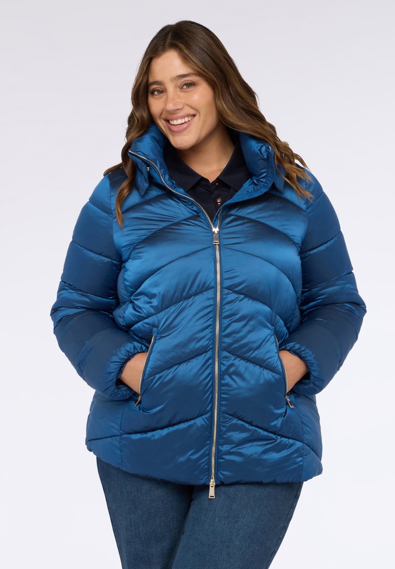 Chaqueta acolchada azul con cremallera frontal, patrón de chevron, cuello alto y bolsillos laterales. El material tiene una textura suave y brillante.