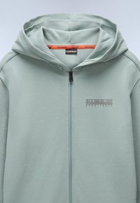 Felpa verde chiaro con zip e cappuccio, caratterizzata da un logo stampato in grigio. Realizzata in tessuto morbido con una texture liscia e un design minimale.