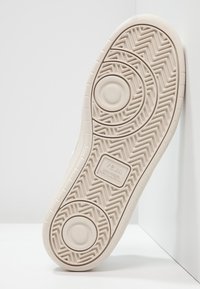 Semelle d’une basket beige VEJA avec des motifs de crampons circulaires et en chevron, nom de la marque et texte « wild rubber from Amazonia » visibles.