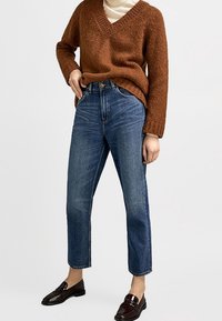 Maglione di maglia marrone con scollo a V, abbinato a jeans blu a vita alta e mocassini scuri. Stile cropped a gamba dritta.
