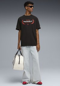 Sort t-shirt med rød "Formula 1" grafik, løse lyseblå jeans og en hvid duffeltaske med sorte accenter. Røde sko fuldender looket.