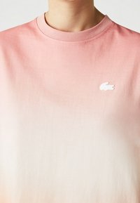 Krátký rukáv gradient tričko v růžové až bílé barvě. Měkká látka, kulatý výstřih, s malým bílým vyšitým logem na hrudi.