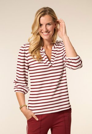 Gestreept shirt met lange mouwen in wit en bordeauxrood met een V-hals en gerimpelde mouwen, gecombineerd met bordeauxrode broek. De stof lijkt licht van gewicht.
