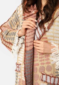 Textúrovaný šál v béžových a ružových odtieňoch, s vzormi bodiek a pruhov, so strapcovými okrajmi a niekoľkými vreckami.