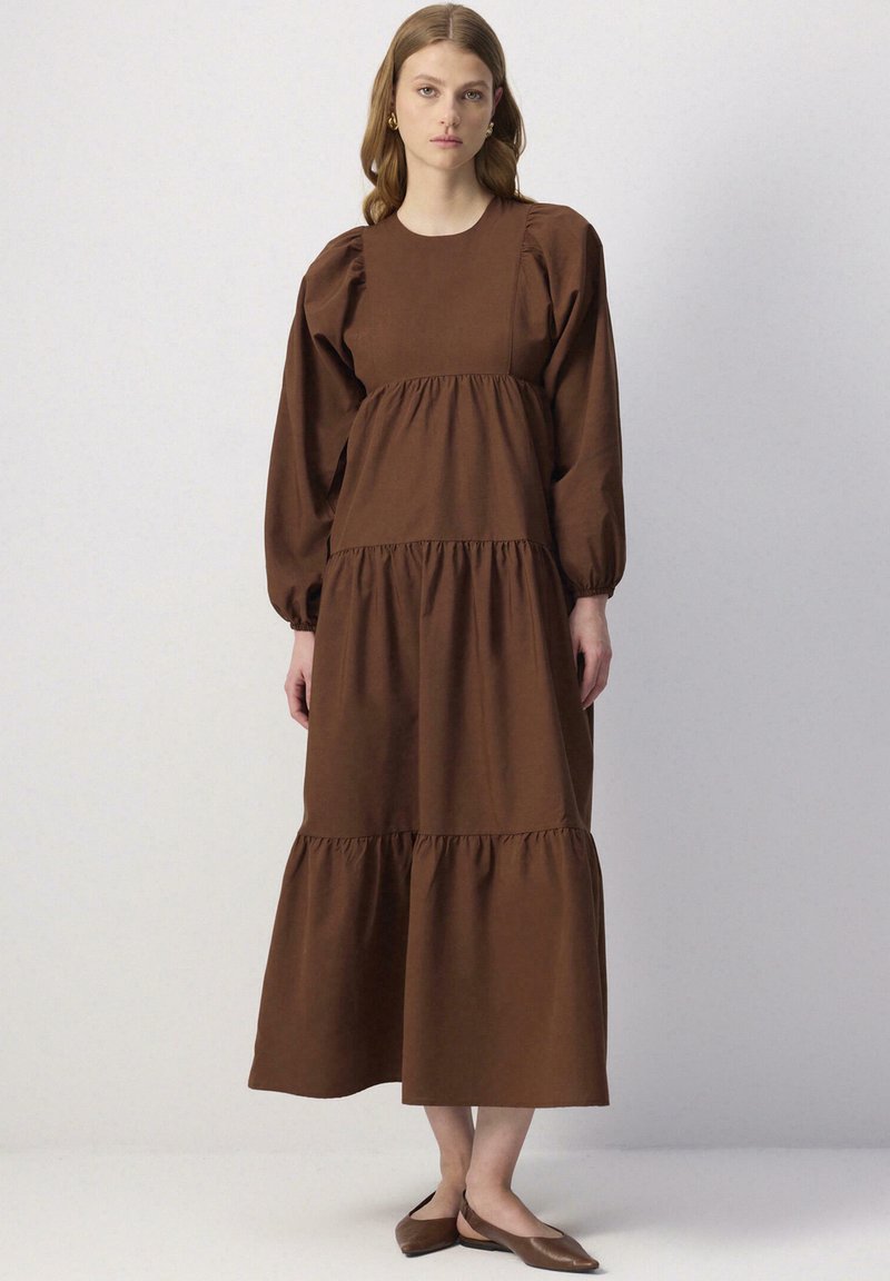 Bruine katoenen maxi-jurk met pofferige mouwen, een gelaagde zoom en een aansluitend lijfje. Bevat elastische Accenten bij de pols en taille voor extra textuur.