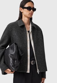 Grijze wollen jas met een rits aan de voorkant, een opstaande kraag en een ontspannen pasvorm. Draag deze over een zwart shirt, gecombineerd met een zwarte leren tas en zonnebril.