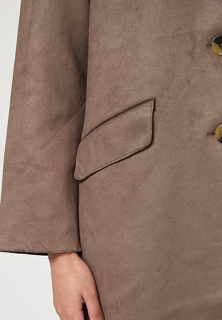 Giacca in suede marrone con una tasca a pattina, bottoni grandi e una vestibilità rilassata con maniche ampie. Texture morbida con una finitura opaca.