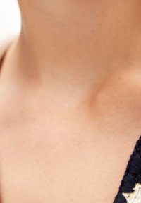 Gros plan sur le cou et le haut de la poitrine d'une personne à la peau claire, portant un vêtement texturé sombre sur le côté droit.