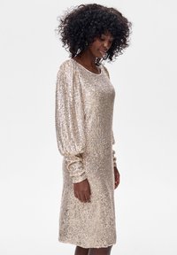 Błyszcząca sukienka z cekinów w kolorze złotym o luźnym kroju, z okrągłym dekoltem i długimi, marszczonymi rękawami, z teksturowaną powierzchnią i długością do kolan.