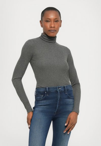 Grå turtleneck topp med lange ermer, laget av et mykt, elastisk stoff. Kombinert med tettsittende blå denimjeans.