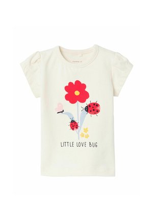 T-shirt a maniche corte color crema con una grafica di un fiore rosso, due coccinelle rosse e il testo "LITTLE LOVE BUG" in nero. Materiale in cotone morbido.