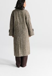 Manteau long en mélange de laine, motif pied-de-poule marron et beige, coupe décontractée, manches larges avec accents de boutons, affiché de dos.