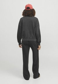 Schwarzer Hoodie und dazu passendeweite Hosen, beide aus weichem Material. Eine rote Baseballmütze rundet das Outfit ab. Keine auffälligen Muster oder Akzente.