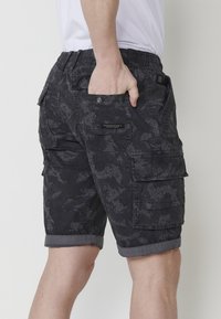Shorts cargo noirs avec un motif texturé, taille élastique, poches multiples et ourlet retroussé. Fabriqué en tissu durable.