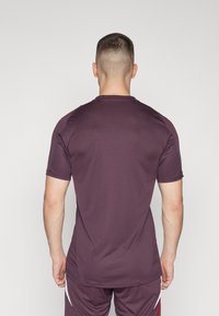 Kortärmad atletisk skjorta i mörk burgundisk tyg med en slät textur. Har en rundad halsringning och kontrasterande detaljer på axlarna.