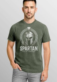Olive green cotton t-shirt featuring a white Spartan helmet graphic with text "SPARTAN" and "PAIN IS TEMPORARY" in distressed font. Short sleeves.
